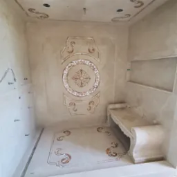 Wykończona łazienka w beżowych tonacjach z dekoracyjnymi wzorami na ścianach, podłodze i suficie. Widoczne eleganckie zdobienia i wnęka w ścianie.