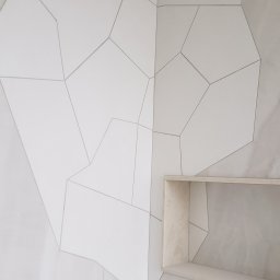 Soldatke Łazienki - Ściana z białych, nieregularnych płytek z szarymi fugami i wnęką. Minimalistyczny design, neutralna kolorystyka. Częściowy widok na ścianę.