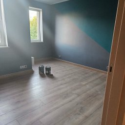 Soldatke Łazienki - Nowocześnie wykończony pokój z geometrycznym malowaniem ścian w szarości i turkusie, jasną podłogą panelową i czarnym oświetleniem szynowym. Na podłodze dwie puszki farby.