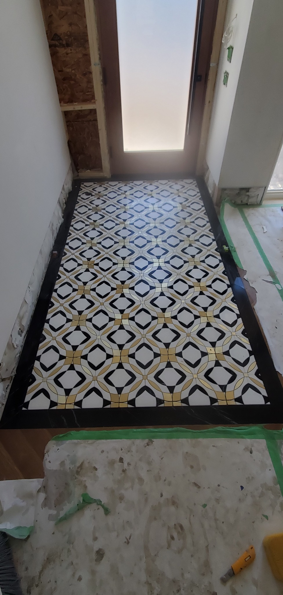 Wzorzysta podłoga z płytek w trakcie układania, widoczne zabezpieczenia i narzędzia. Nietypowy wzór z motywem rombów i złotymi akcentami.