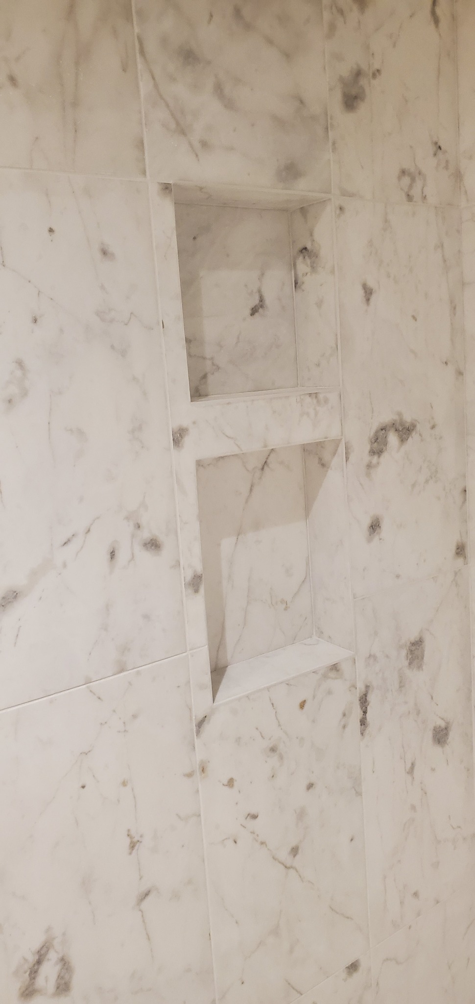 Wykończona wnęka w ścianie z marmurowych płytek w Wejherowie. Dwie kwadratowe półki, jasne, eleganckie wykończenie. Detal łazienki.