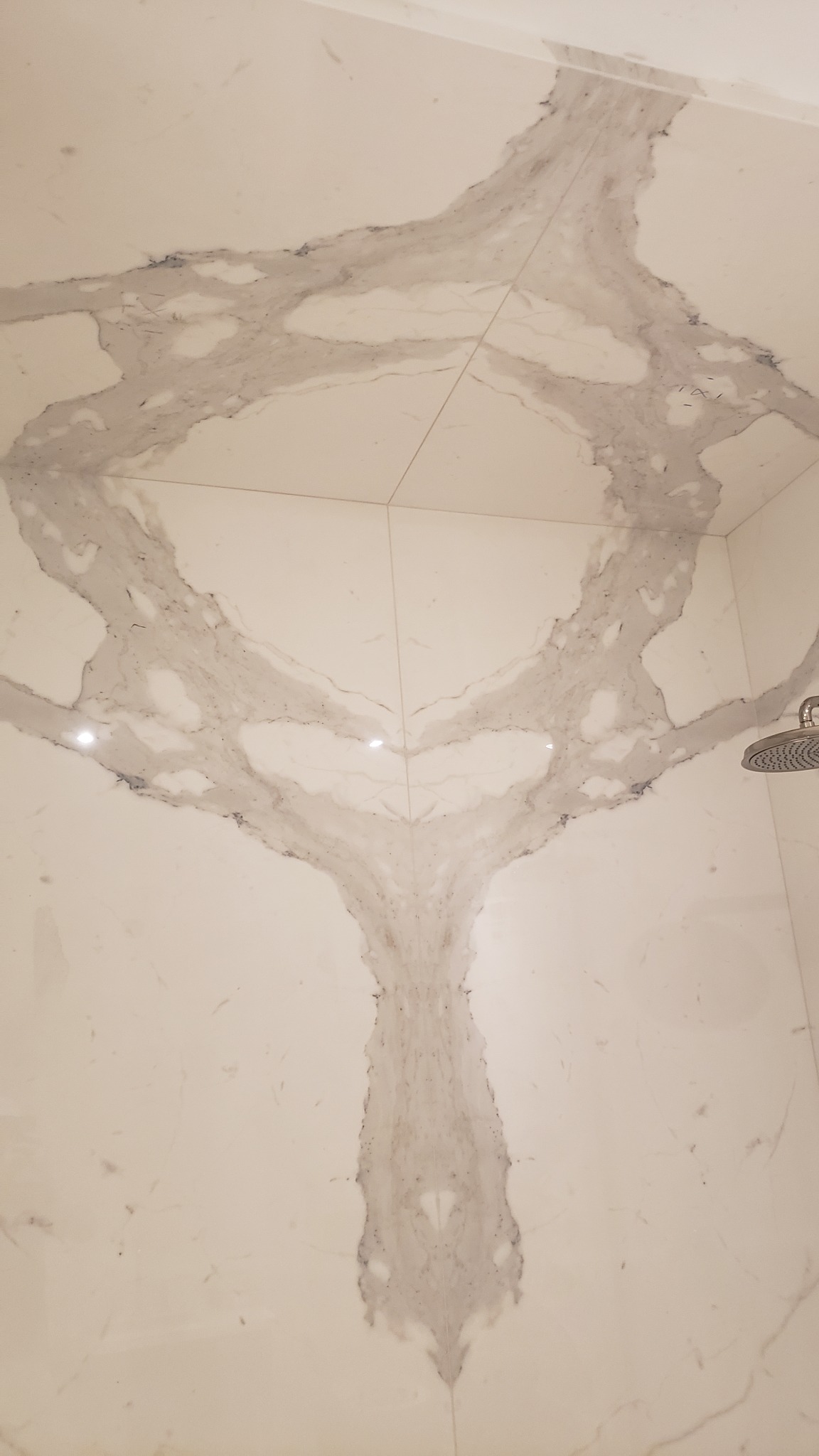 Wykończona kabina prysznicowa z białych płytek imitujących marmur z szarymi żyłami, z widoczną słuchawką prysznicową po prawej stronie.