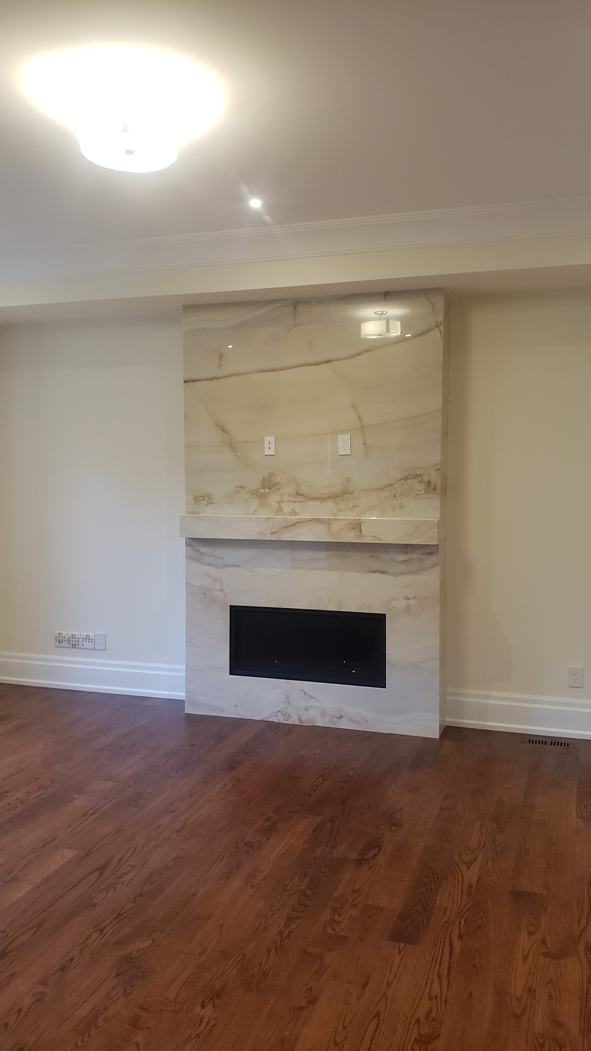 Elegancki kominek z marmurowym wykończeniem, wkomponowany w jasne wnętrze z drewnianą podłogą. Nowoczesny design z subtelnym oświetleniem sufitowym.