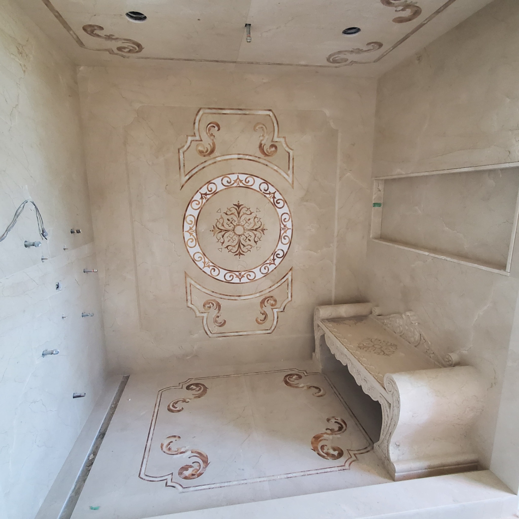 Wykończona łazienka w beżowych tonacjach z dekoracyjnymi wzorami na ścianach, podłodze i suficie. Widoczne eleganckie zdobienia i wnęka w ścianie.