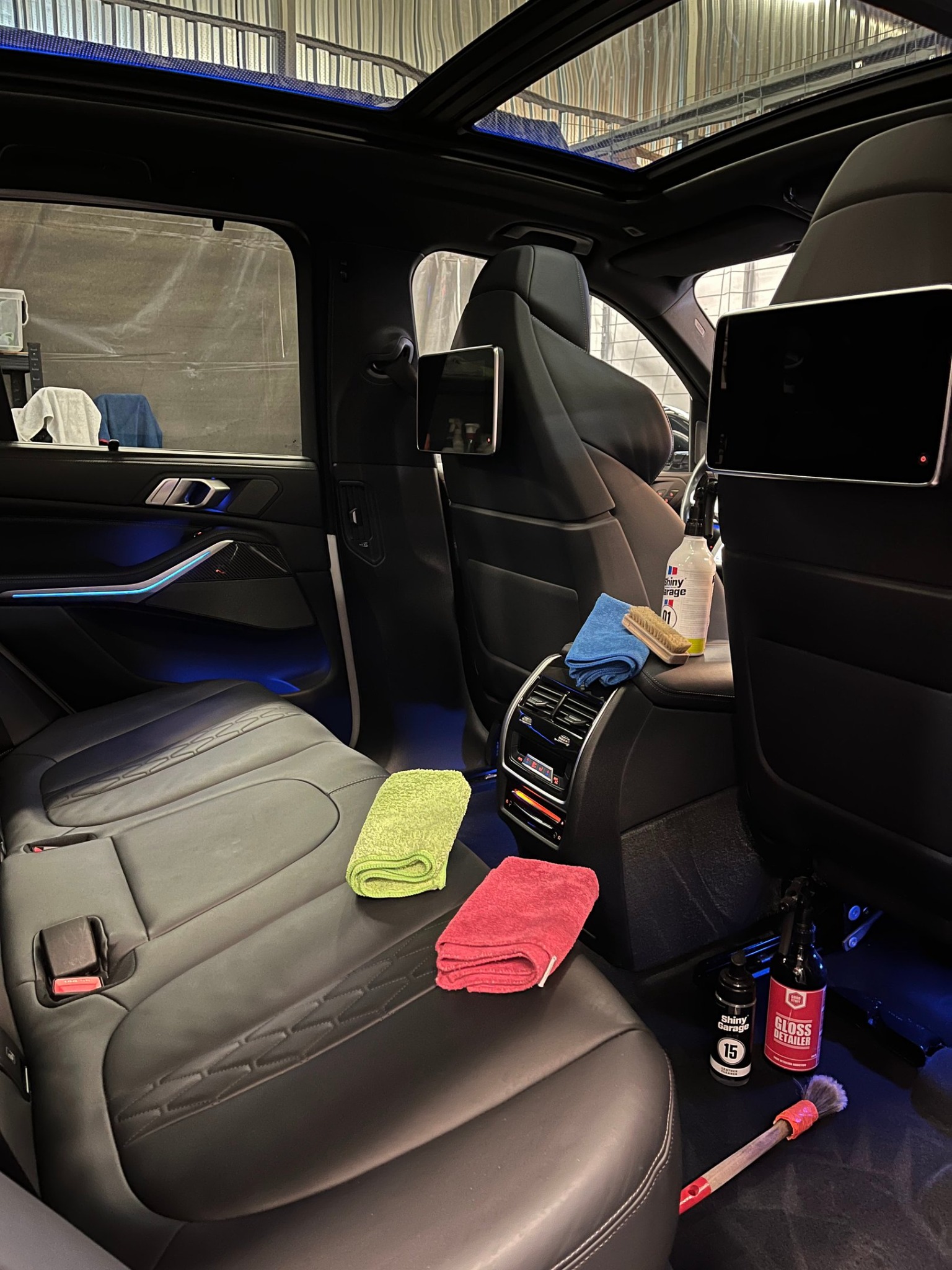 Wnętrze luksusowego BMW X5 po detailingu: czarna skórzana tapicerka z zieloną i czerwoną mikrofibrą, środki czyszczące Shiny Garage, widok z tylnej kanapy.