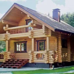 Dwukondygnacyjny dom z bali z balkonem, ciemna dachówka i metalowy komin, otoczony zielenią.