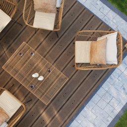 GREENCRAFT NATALIA SWEBODZIŃSKA - Z góry: rattanowe meble ogrodowe (krzesła z poduszkami, stolik z napojami) na drewnianym tarasie, obok trawnik i kamienna ścieżka. Minimalistyczny design.