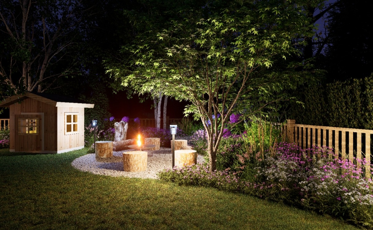 Oświetlony ogród nocą z paleniskiem otoczonym siedziskami z pniaków, drewnianym domkiem dla dzieci i kwitnącymi rabatami wzdłuż ogrodzenia.