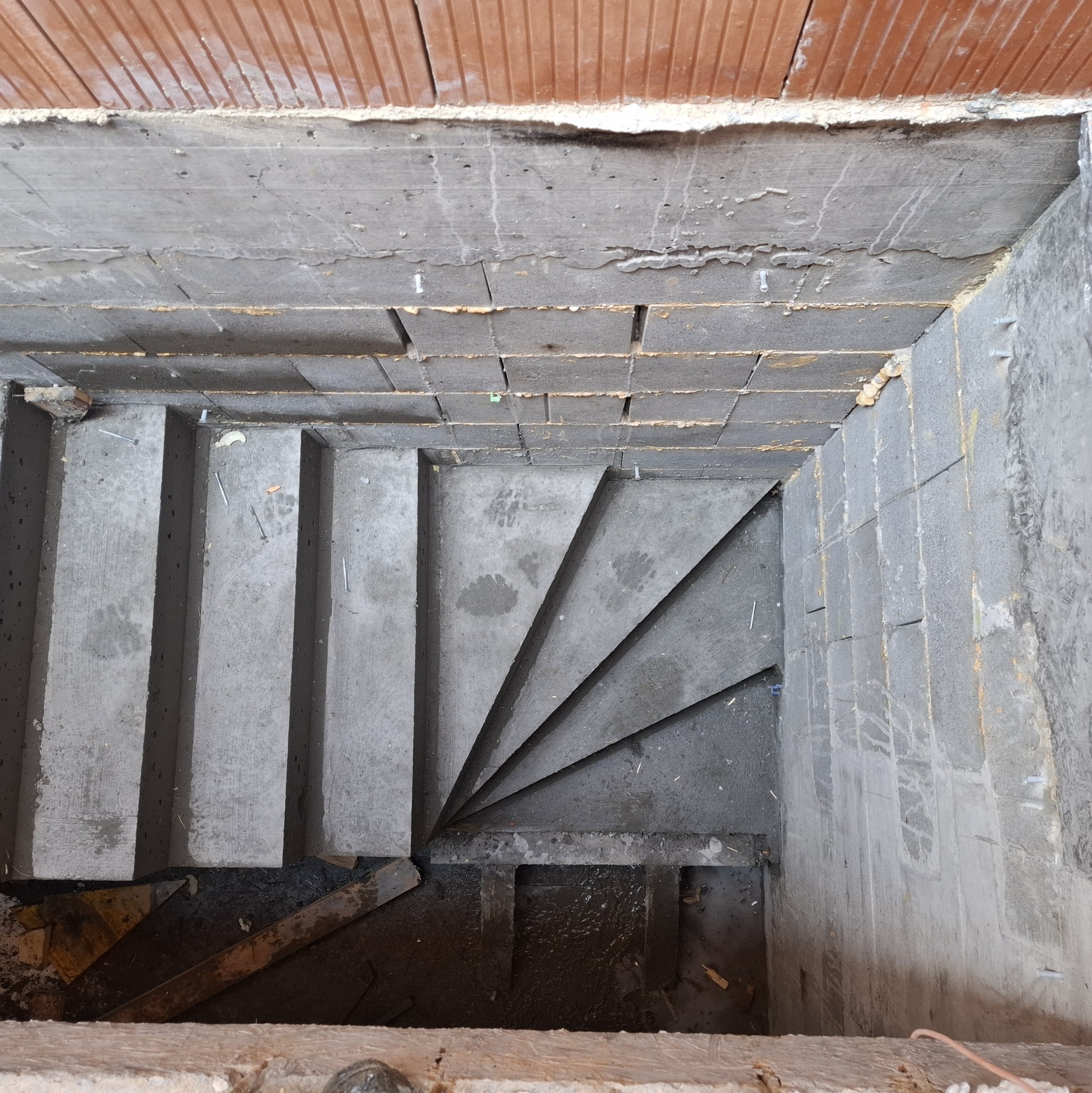 Surowe, betonowe schody w trakcie budowy, widok z góry. Widoczne ślady po pracy, szalunki i fragmenty ceglanego stropu.