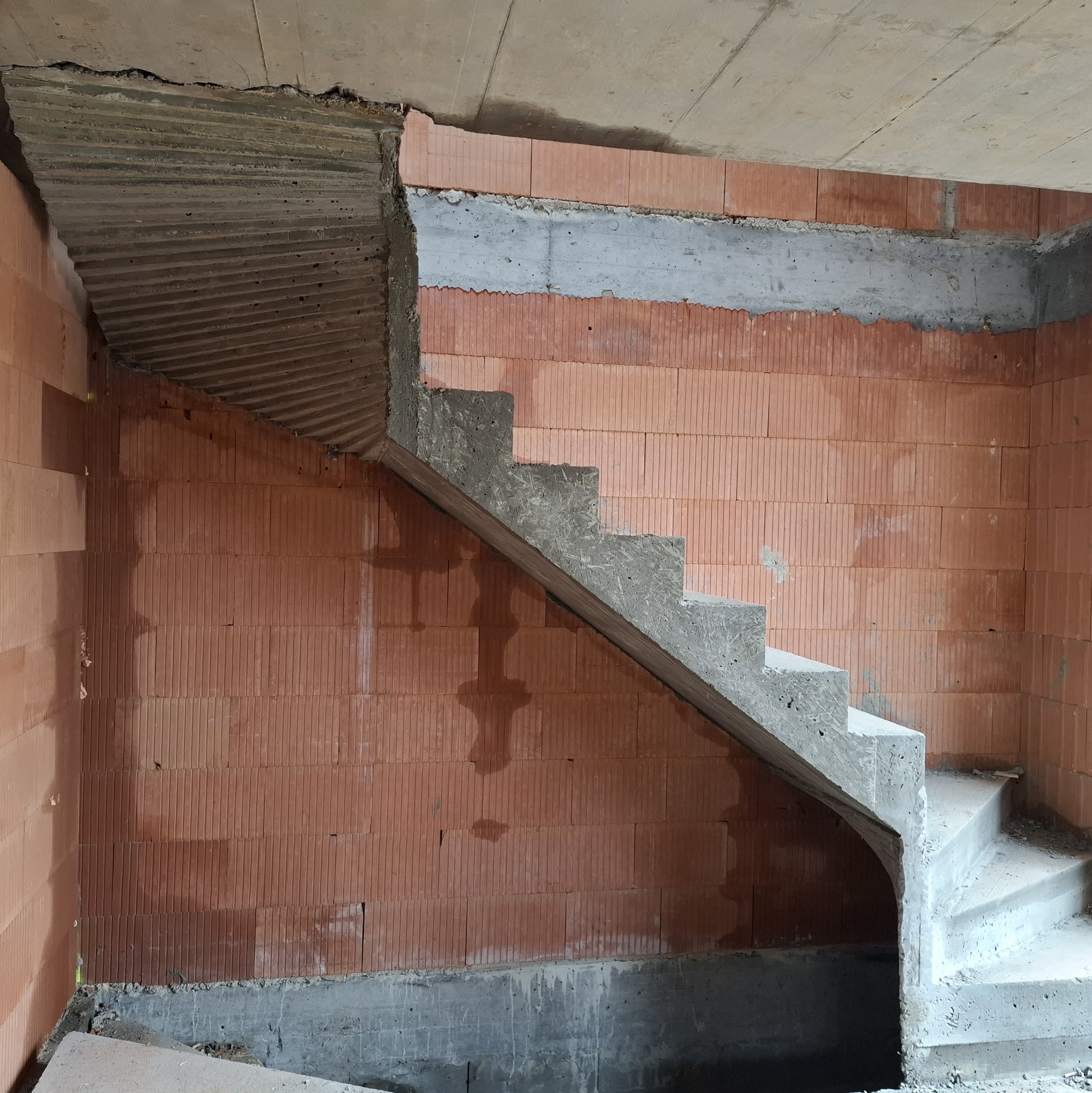 Surowe schody betonowe w trakcie budowy, widoczne cegły i betonowe elementy konstrukcyjne. Kąt ujęcia podkreśla surowość i etap budowy.