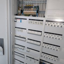 ENCEL ELECTRO SPÓŁKA Z OGRANICZONĄ ODPOWIEDZIALNOŚCIĄ - Rozdzielnia elektryczna GIRA z bezpiecznikami, modułami KNX i okablowaniem. Widoczne białe przewody i szyny DIN. Panel sterowania z opisami i oznaczeniami.