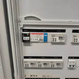 Panel sterowania inteligentnego domu GIRA z modułami KNX i DALI, widoczne bezpieczniki i oznaczenia stref: Bel Fläche, I Flur/WC I. Elementy automatyki w szarej szafie.