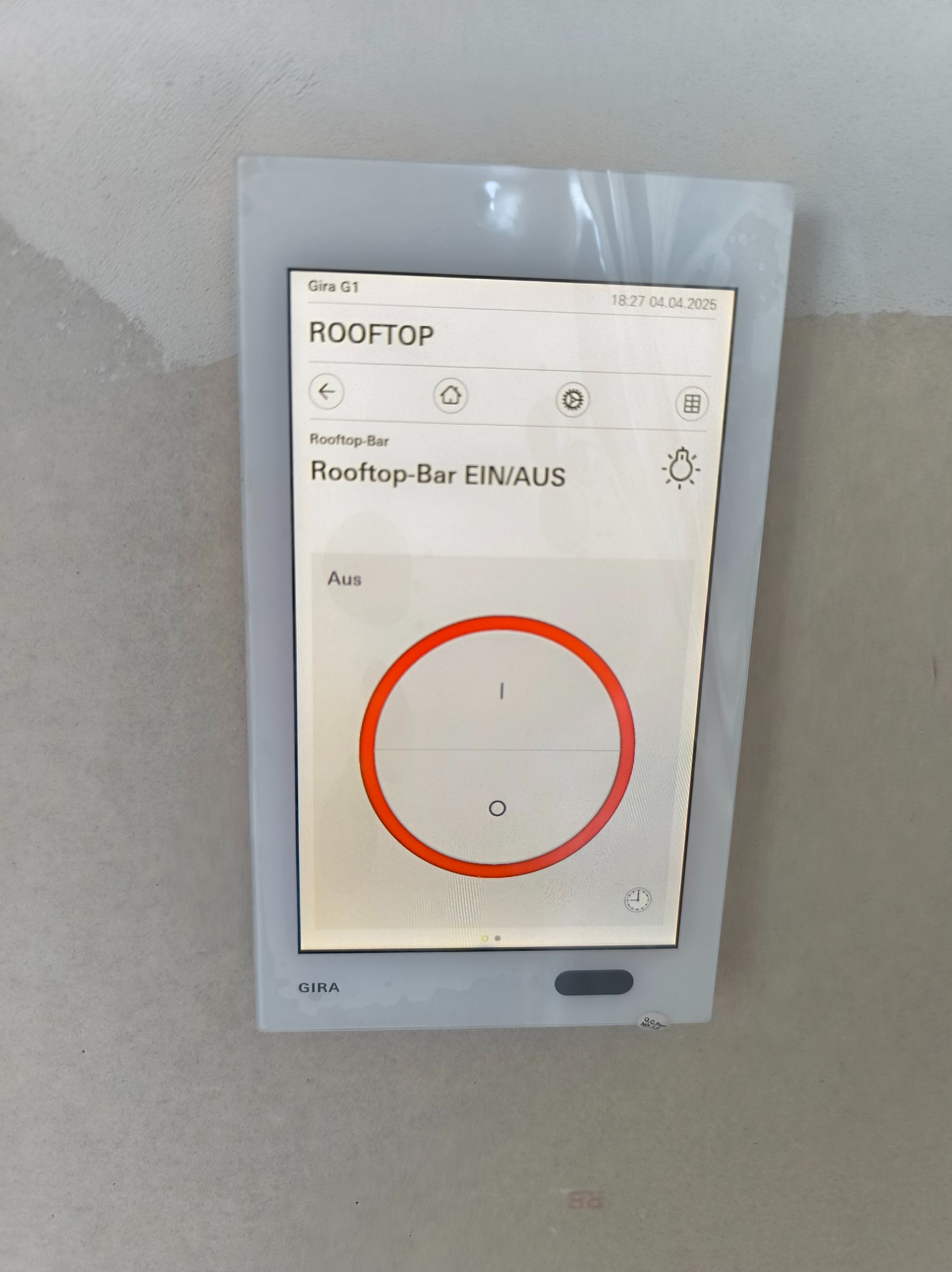 Panel sterowania Gira G1 zamontowany na ścianie, wyświetlający interfejs systemu inteligentnego domu z opcją włączania/wyłączania strefy 'Rooftop-Bar'.