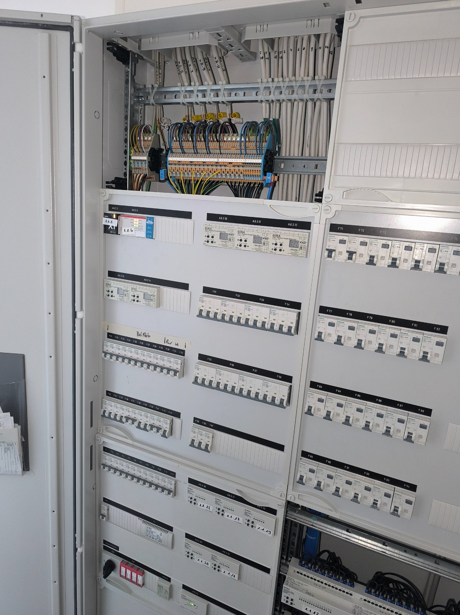 Rozdzielnia elektryczna GIRA z bezpiecznikami, modułami KNX i okablowaniem. Widoczne białe przewody i szyny DIN. Panel sterowania z opisami i oznaczeniami.