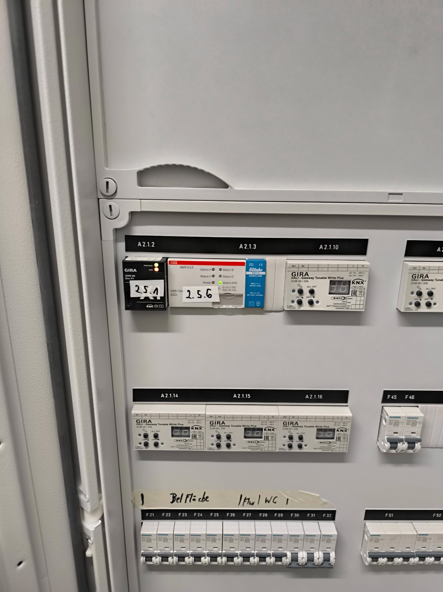 Panel sterowania inteligentnego domu GIRA z modułami KNX i DALI, widoczne bezpieczniki i oznaczenia stref: Bel Fläche, I Flur/WC I. Elementy automatyki w szarej szafie.
