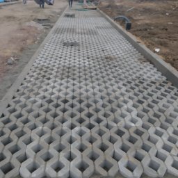 Marek Wieczorkiewicz - Fragment układania ażurowej kostki brukowej na podbudowie. W tle pracownicy i materiały budowlane.