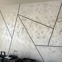 Złota Rączka Kraków - Dekoracyjna ściana w odcieniach szarości z geometrycznym wzorem. Na podłodze widoczne narzędzia i skrzynki monterskie.
