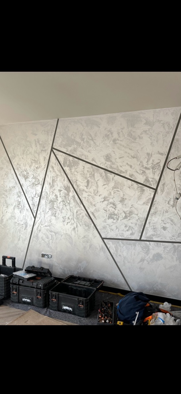 Dekoracyjna ściana w odcieniach szarości z geometrycznym wzorem. Na podłodze widoczne narzędzia i skrzynki monterskie.