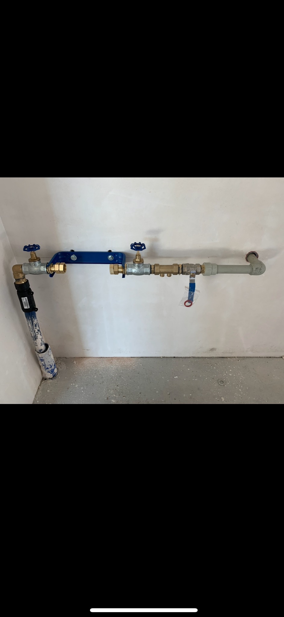 Kompleksowa instalacja wodna z zaworami kulowymi i rurami z tworzywa, zamontowana przy ścianie w surowym stanie. Rury w kolorze szarym i niebieskim.