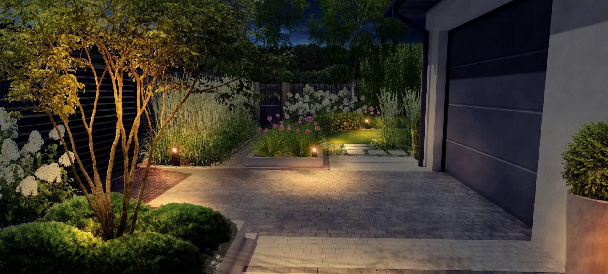 Oświetlony ogród nocą z podjazdem z kostki, rabatami kwiatowymi i dekoracyjnymi trawami. Minimalistyczne lampy ogrodowe podkreślają kompozycję roślin.