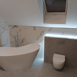 King's Home - Nowoczesna łazienka na poddaszu z wolnostojącą wanną, marmurowymi płytkami i podświetleniem LED. Uwagę zwraca okno dachowe wkomponowane w skos.