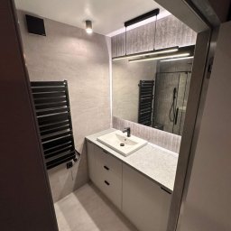 King's Home - Nowoczesna łazienka z umywalką nablatową, grzejnikiem drabinkowym i podświetlanym lustrem. Minimalistyczny design, szare płytki i białe meble.