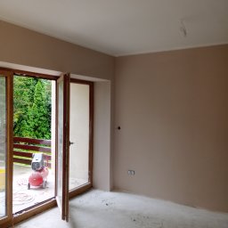 Mariusz Wysocki - Pokój po malowaniu na beżowo z otwartym balkonem. Widoczny kompresor, ślady farby na podłodze, gniazdka elektryczne. Świeżo pomalowane ściany.