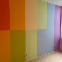 Tomasz Lisek - Ściana pomalowana w pionowe pasy w różnych kolorach tęczy, od czerwieni po fiolet, z widocznym oknem i zabezpieczoną podłogą. Nowoczesne wykończenie wnętrza.