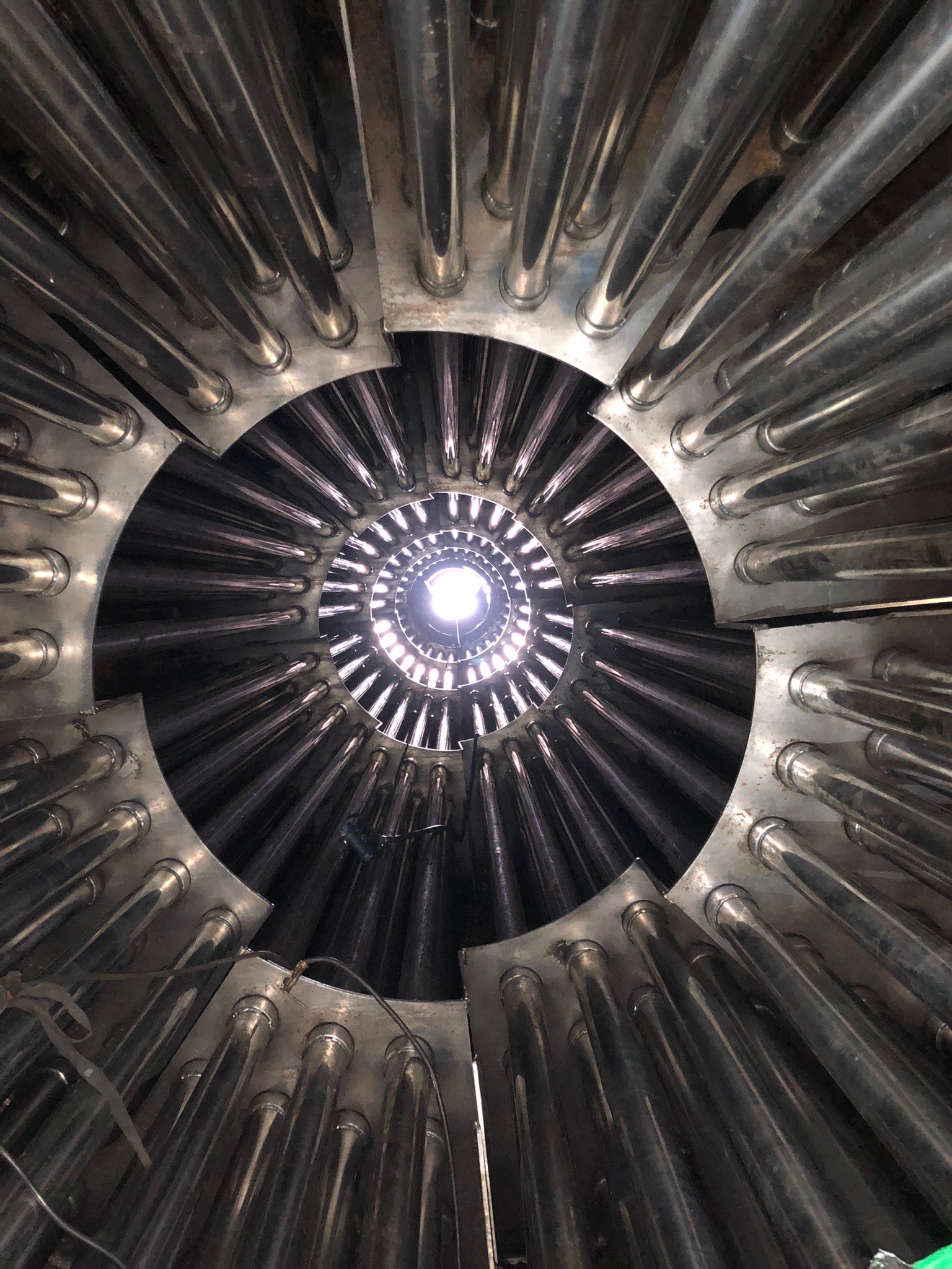 Wnętrze konstrukcji z rur stalowych, ułożonych promieniście wokół centralnego otworu z widocznym źródłem światła. Widok z perspektywy wnętrza konstrukcji.