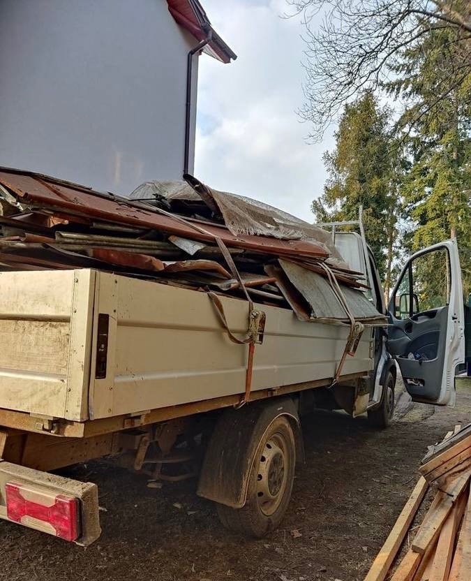 Ciężarówka wypełniona gruzem budowlanym i elementami dachu, zaparkowana na zewnątrz, z otwartymi drzwiami kierowcy, gotowa do wywozu odpadów.