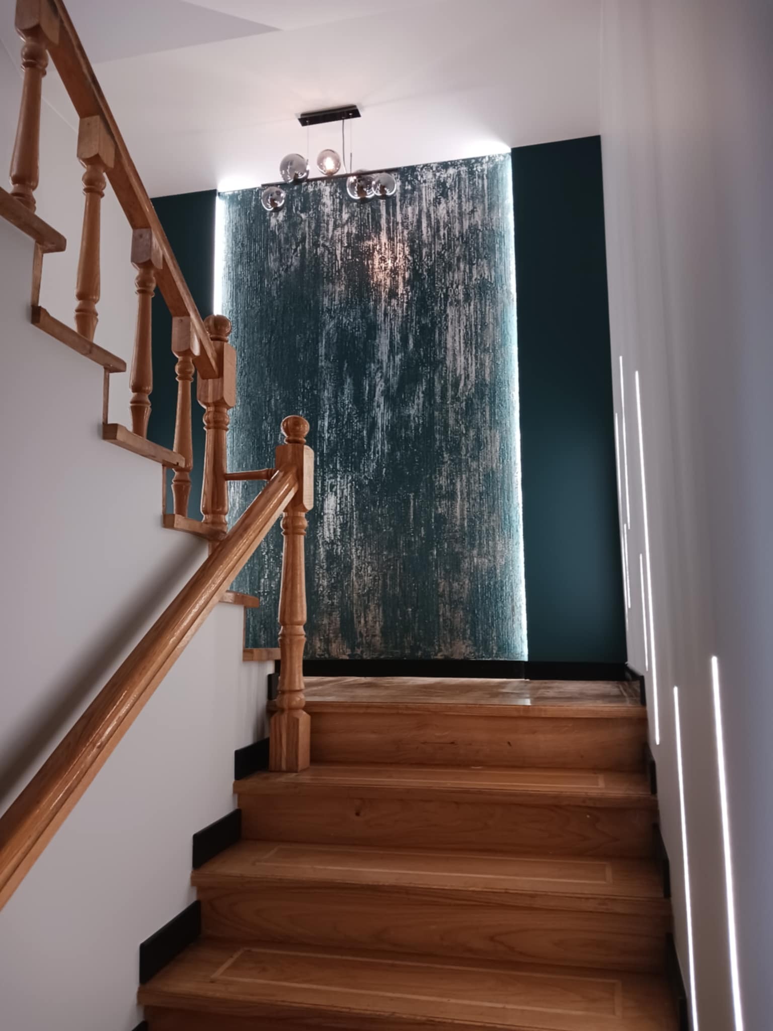 Drewniane schody z balustradą i oświetleniem LED na ścianie w tle. Elementy dekoracyjne i nowoczesna lampa wisząca.