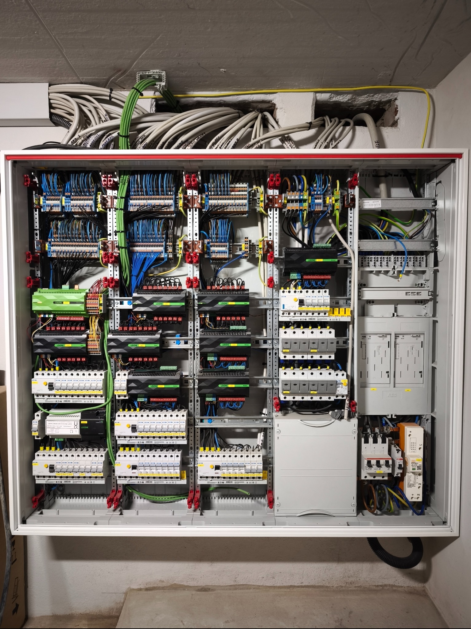 Rozbudowana, profesjonalnie wykonana instalacja elektryczna w skrzynce rozdzielczej z licznymi przewodami, modułami i zabezpieczeniami. Widoczne elementy Loxone i ABB.
