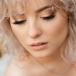 Weronika Kunek - Portret kobiety z blond kręconymi włosami, delikatnym makijażem i srebrnym naszyjnikiem. Zamknięte oczy, skupienie na detalu urody. Naturalne światło.