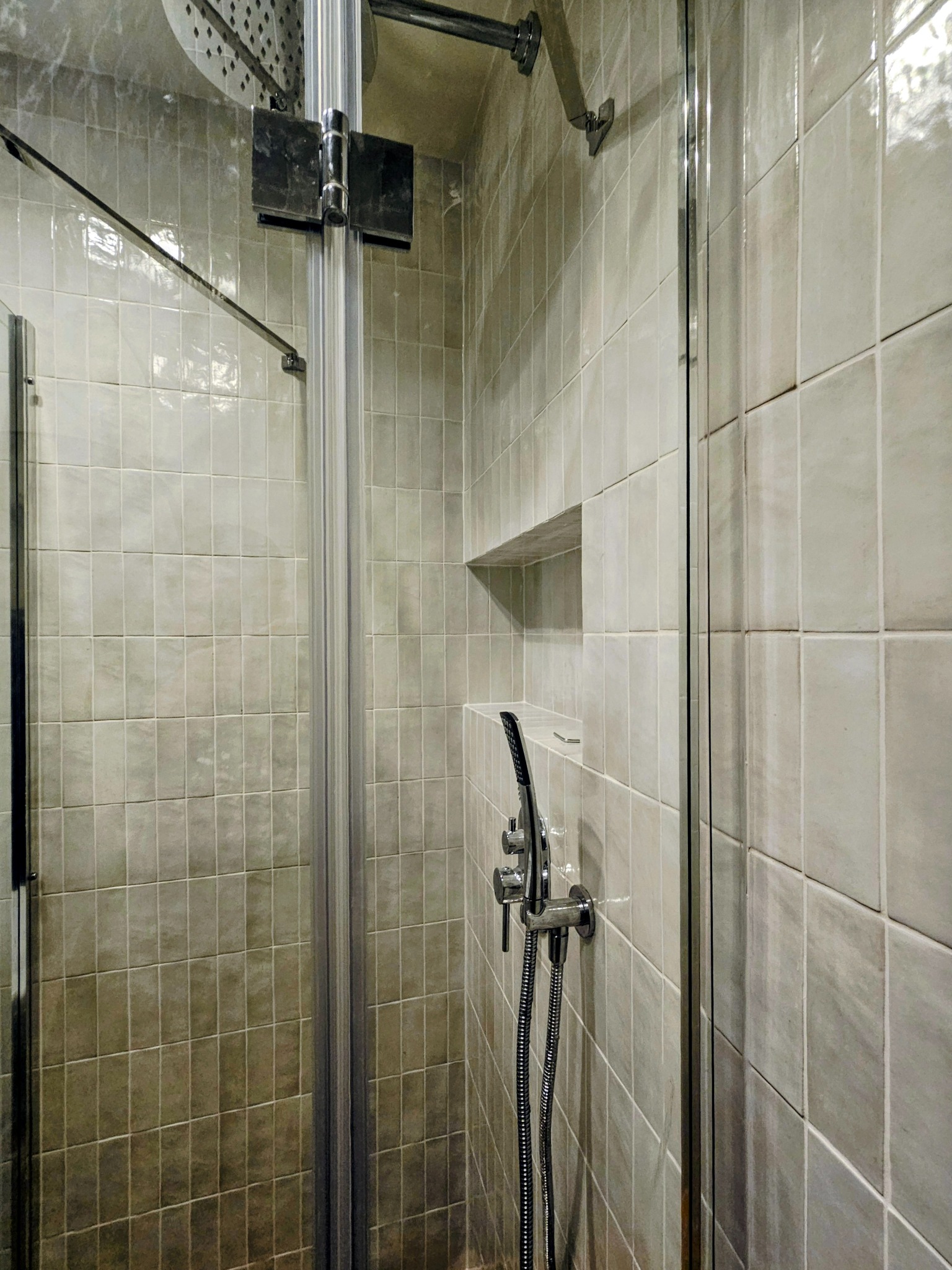 Nowoczesna kabina prysznicowa z szarymi, kwadratowymi płytkami w łazience w Warszawie. Widoczny chromowany zestaw prysznicowy i wnęka w ścianie.