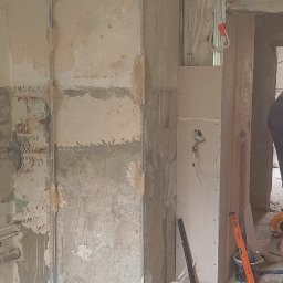 Przemysław Pietrzak - Wnętrze w trakcie remontu. Widoczne ściany z fragmentami starej farby, częściowo pokryte gładzią, oraz zamontowana płyta karton-gips. Przewody elektryczne i narzędzia.