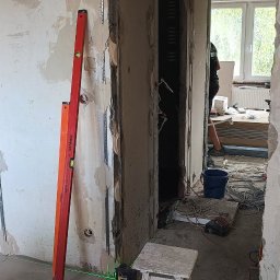 Przemysław Pietrzak - Montaż profili do płyt gipsowo-kartonowych na ścianie z widocznymi łatami szpachli, poziomice, oraz narzędzia w tle. Prace remontowe w trakcie realizacji.