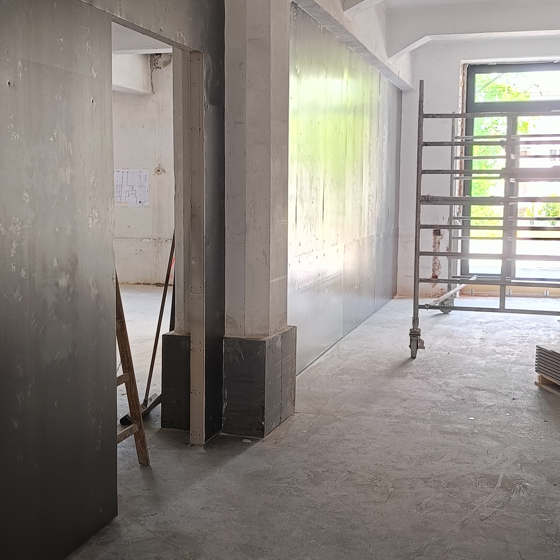 Wnętrze w trakcie remontu: ściany wyłożone płytami, widoczne rusztowanie, narzędzia i surowy beton. Przygotowanie do dalszych prac wykończeniowych.