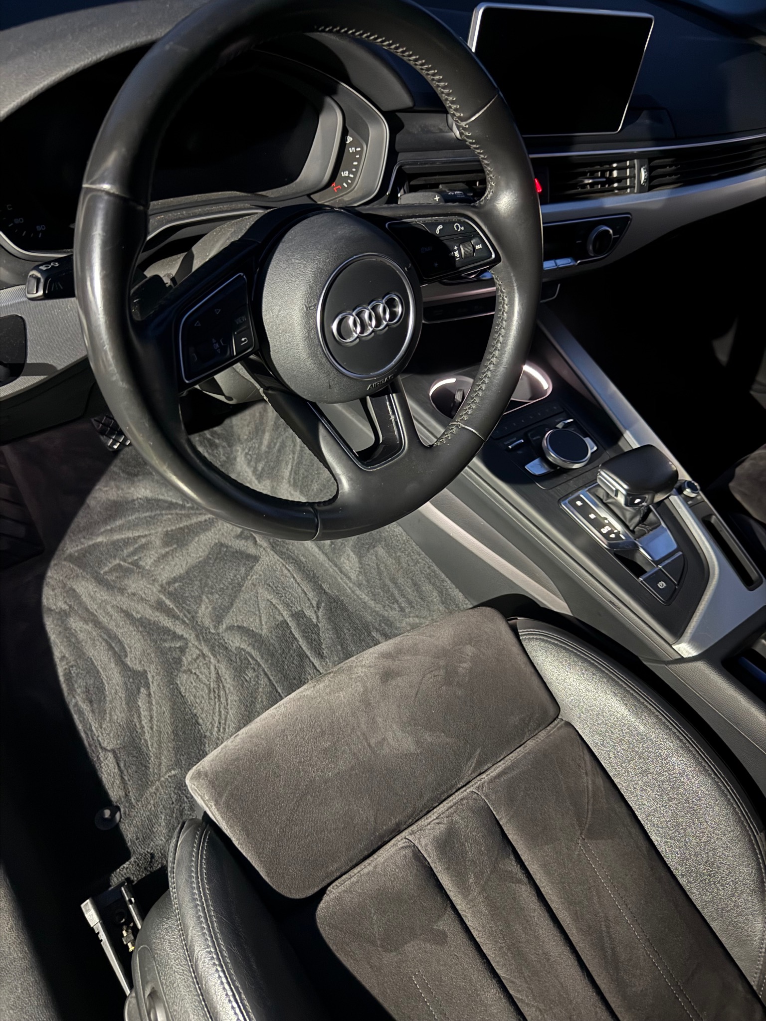 Wnętrze Audi A4: czarna kierownica, deska rozdzielcza, automatyczna skrzynia biegów i wyprana, ciemnoszara tapicerka fotela kierowcy z wyraźnym wzorem.