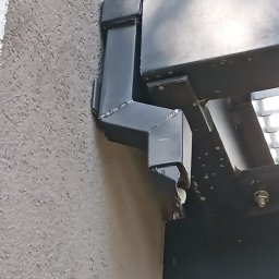 Rynienka z rurą spustową między schodami a budynkiem żeby zapobiec brudzeniu elewacji.