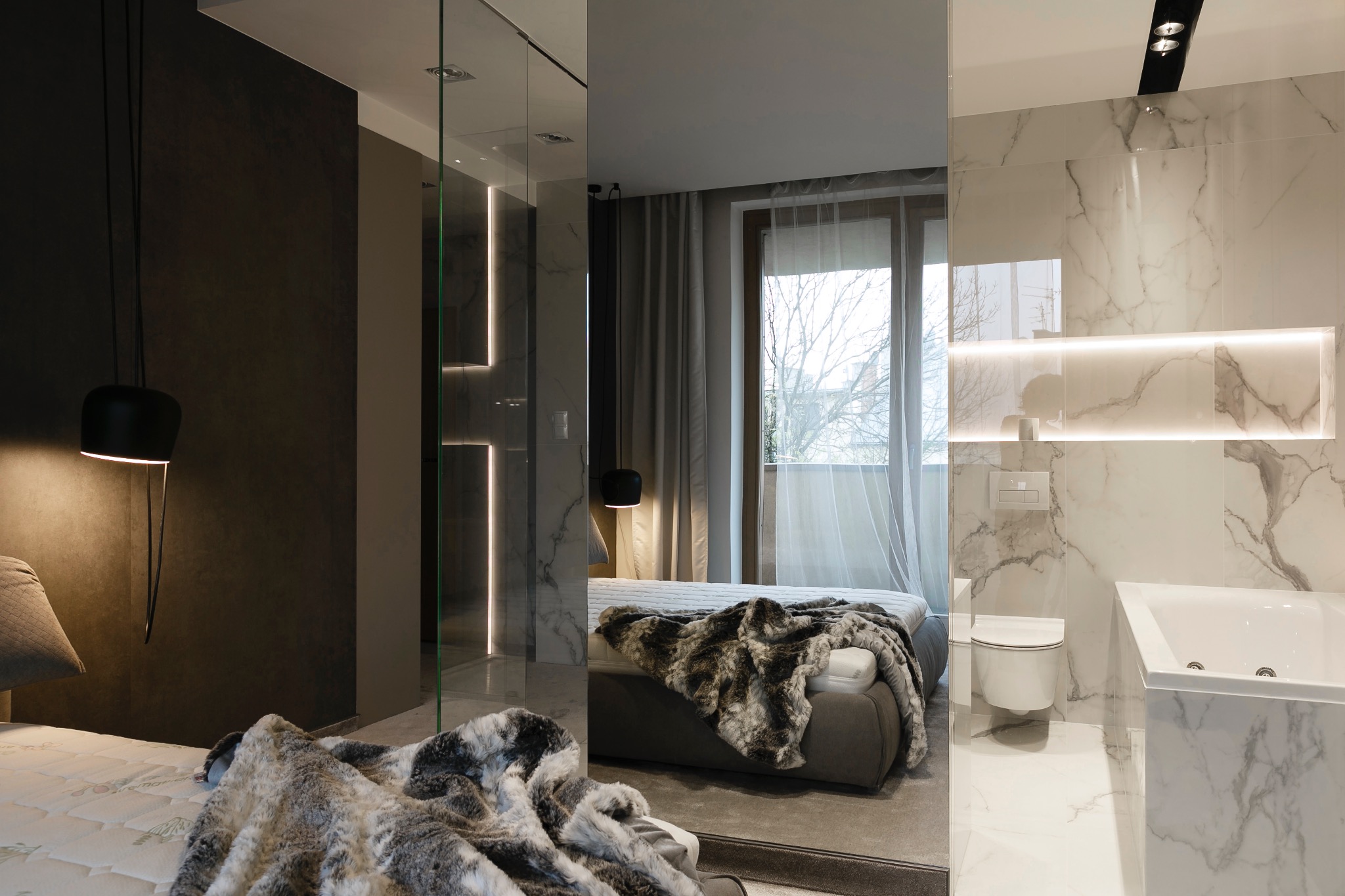 Elegancka sypialnia z łazienką: marmurowe ściany, szklana kabina prysznicowa z oświetleniem LED, minimalistyczne lampy i tekstylia w odcieniach szarości. Nowoczesny design.