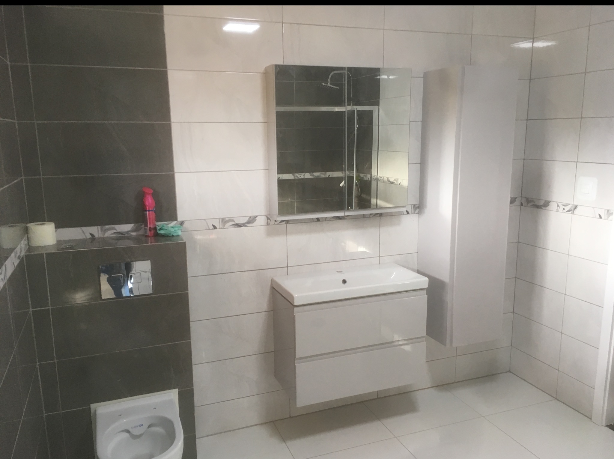 Nowoczesna łazienka po remoncie w Wałbrzychu: białe i szare płytki, umywalka z szafką, lustro z oświetleniem i wisząca szafka, tworzące spójną całość.