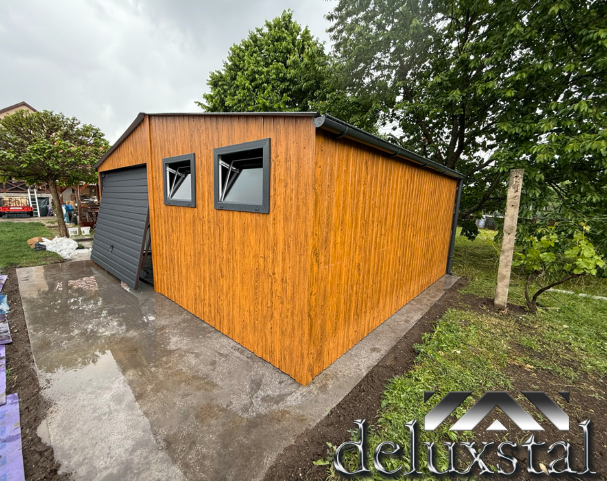 Blaszany garaż w kolorze złotego dębu z bramą uchylną, dwoma oknami PCV i dodatkowymi drzwiami. Widoczne okucia narożne i rynna.