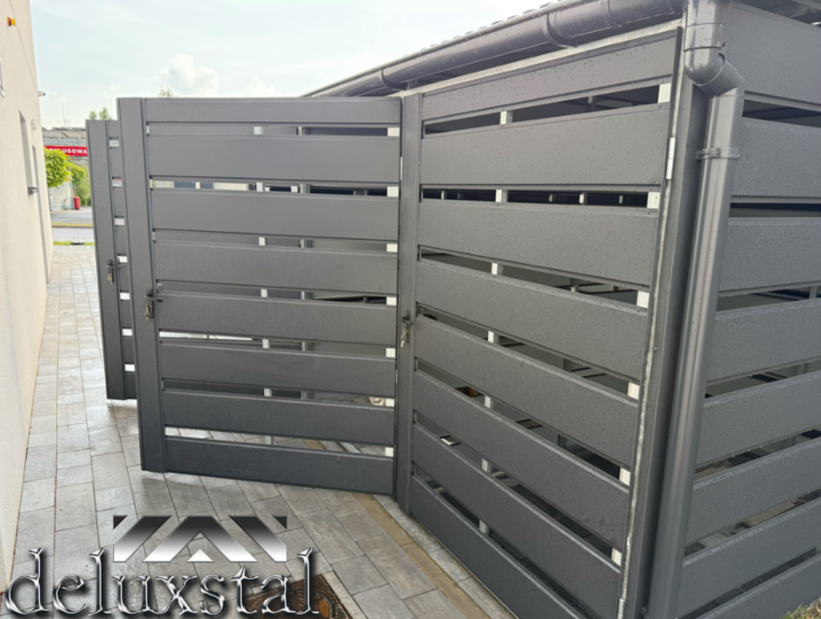 Nowoczesna, grafitowa brama garażowa z poziomymi panelami, częściowo otwarta, z widocznym systemem odprowadzania wody deszczowej i kostką brukową.