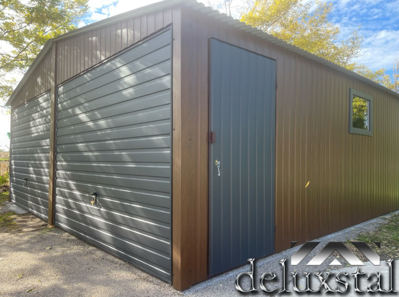 Nowoczesny garaż blaszany z dwiema bramami segmentowymi w kolorze szarym i drzwiami wejściowymi w odcieniu grafitu, z oknem po prawej stronie i elementami wykończeniowymi w kolorze drewna.