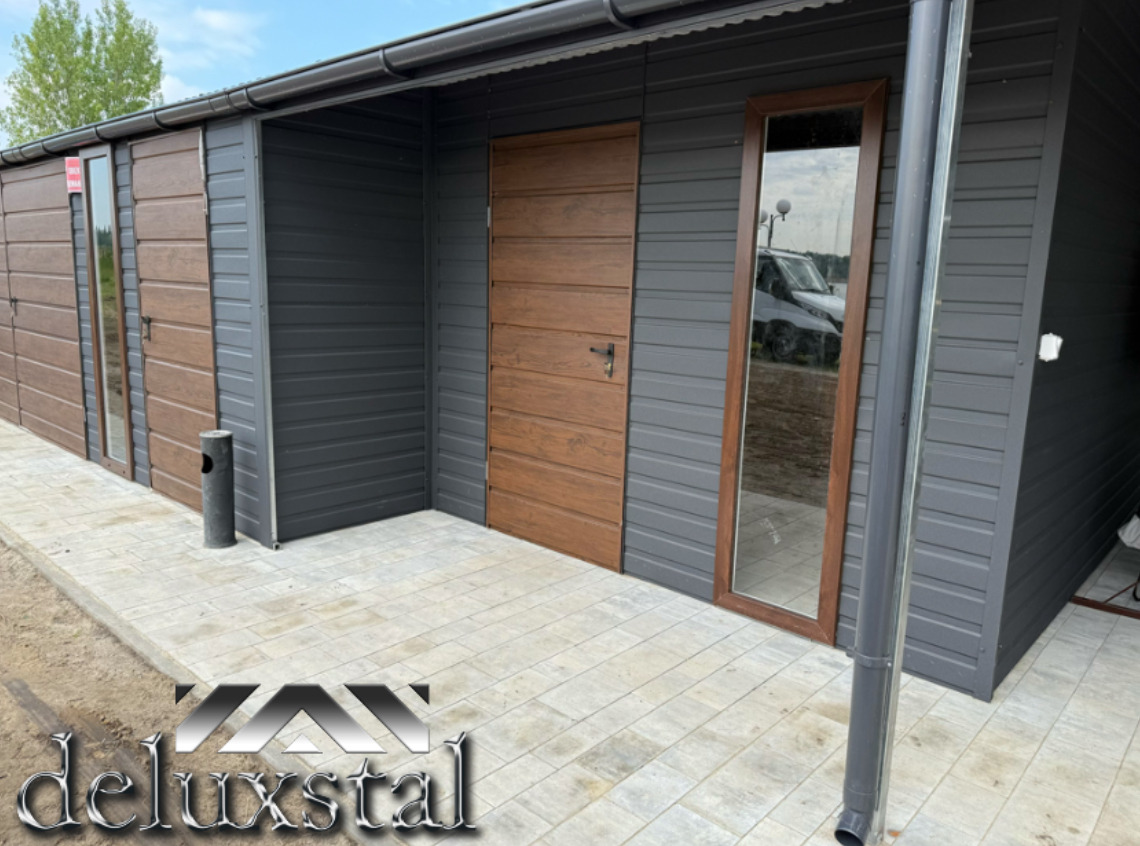 Nowoczesny garaż z blachy w odcieniach szarości i brązu, z drewnopodobną bramą i oknem. Widoczny fragment chodnika z kostki brukowej i rynna.