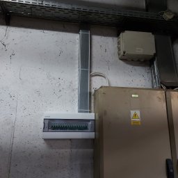 MD BUD - Szara skrzynka rozdzielcza z przewodami na ścianie w Łasku. Widoczna tabliczka ostrzegawcza i koryto kablowe.