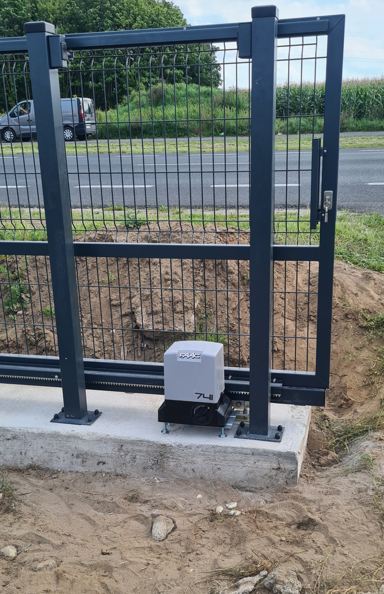 Nowoczesna, przesuwna brama panelowa z automatyką FAAC 741, zamontowana na betonowej podstawie. Widoczne elementy konstrukcyjne i mechanizm napędowy. Tło: droga i zieleń.