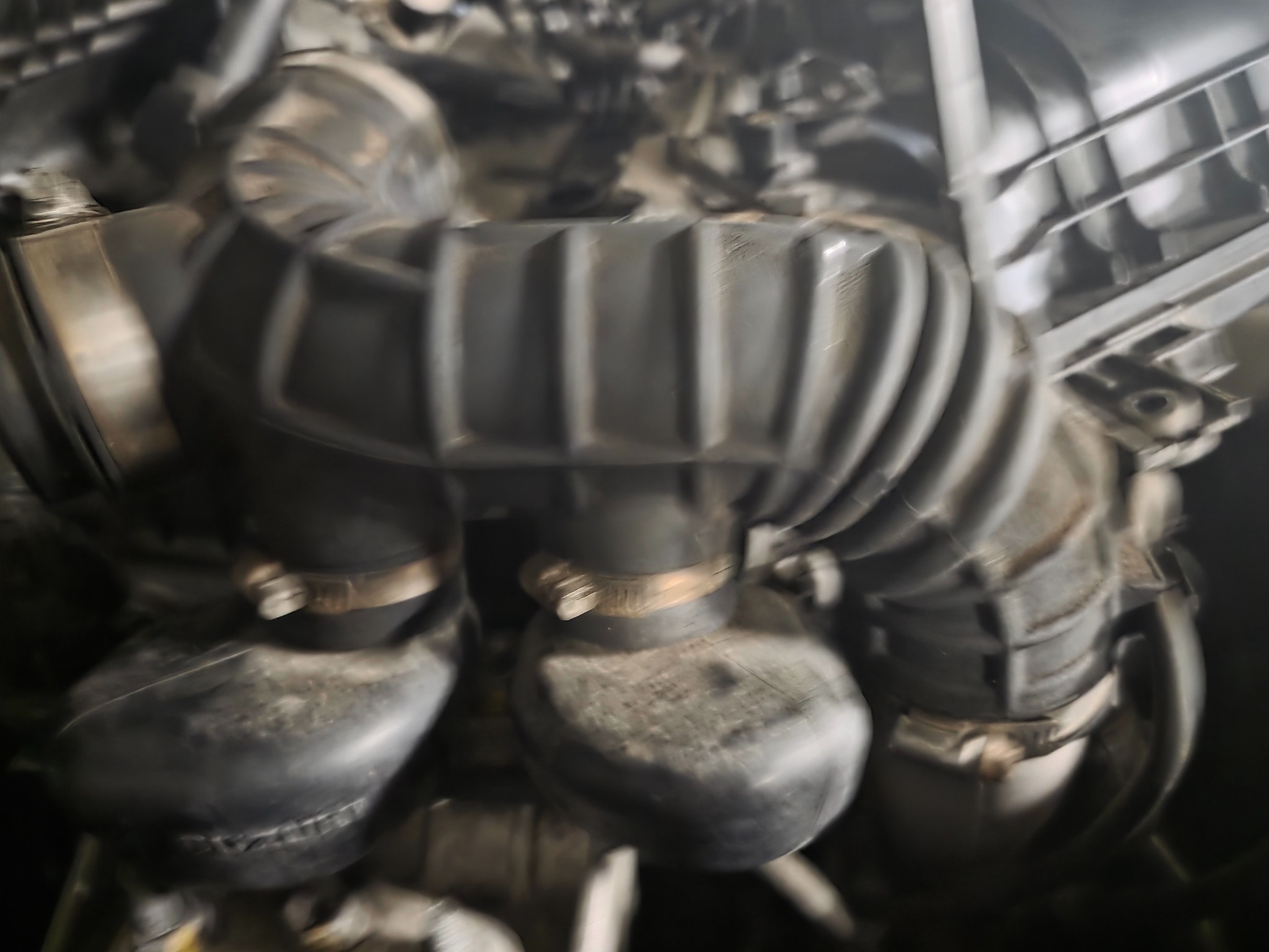 Silnik samochodowy z widocznymi gumowymi przewodami i metalowymi zaciskami, ukazujący fragment układu dolotowego powietrza w komorze silnika.