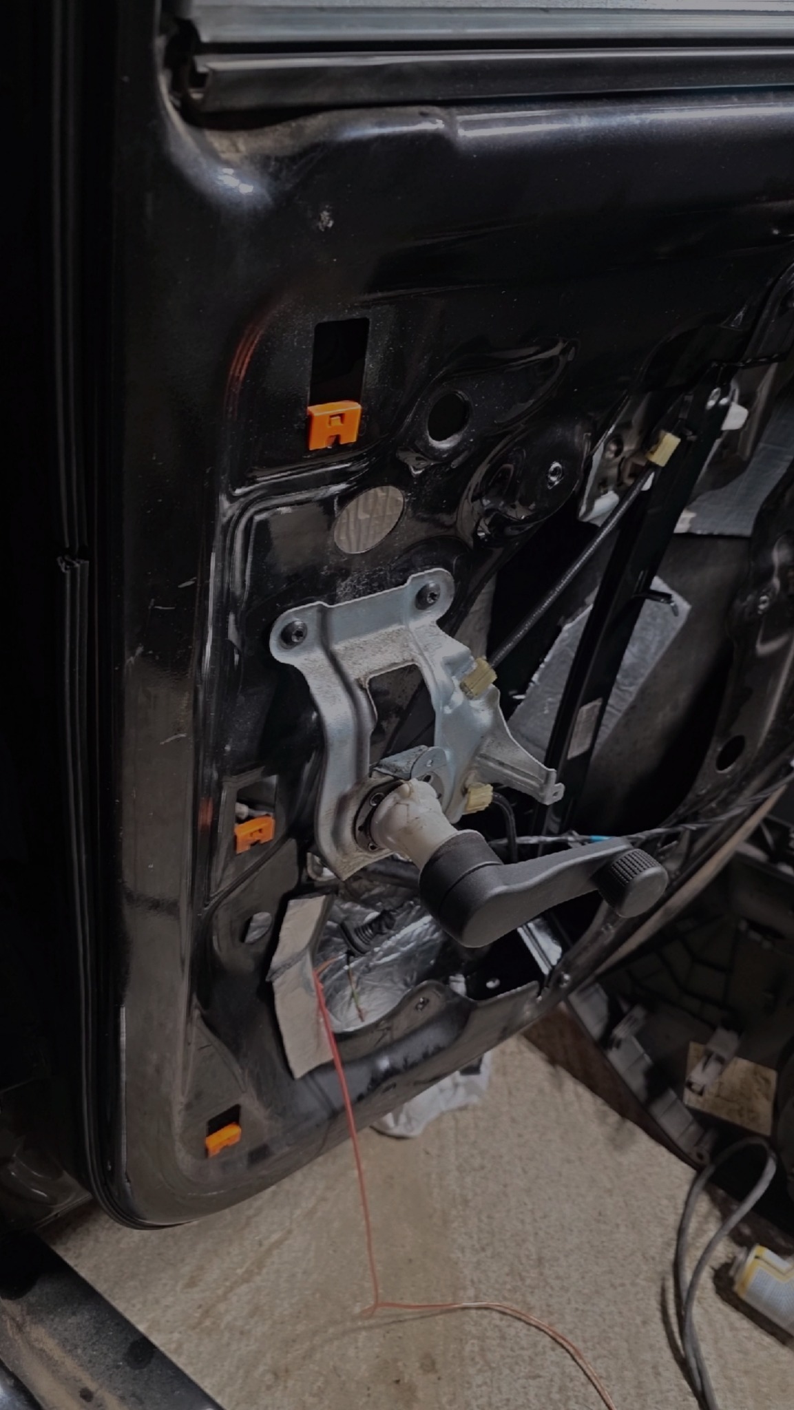 Wnętrze czarnych drzwi samochodowych z widocznym mechanizmem zamka i klamki, elementy tapicerki zdemontowane, widoczne pomarańczowe klipsy mocujące.