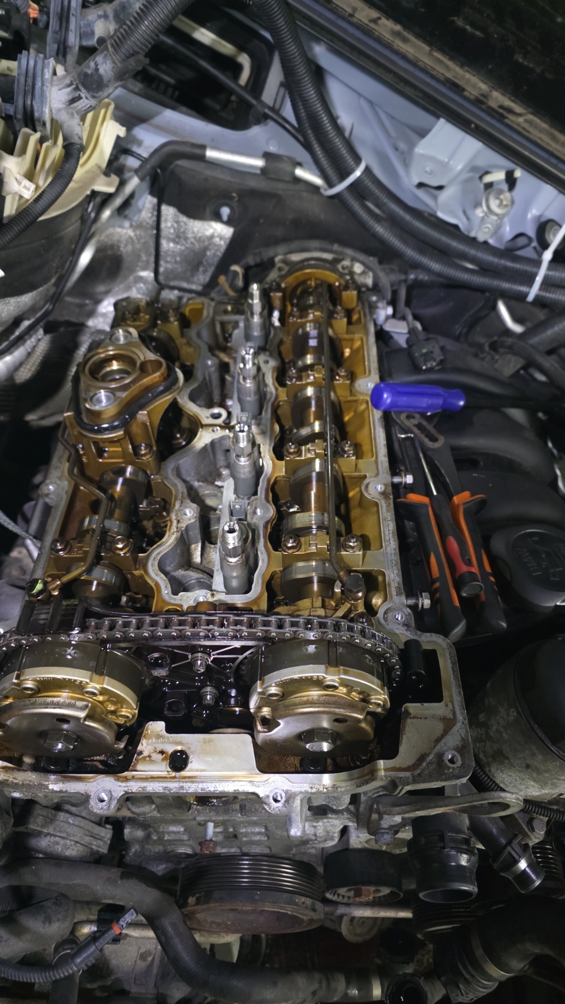 Otwarty silnik samochodowy z widocznymi elementami wewnętrznymi, narzędzia obok. Widok z góry na skomplikowaną konstrukcję w trakcie naprawy lub konserwacji.